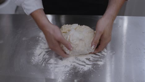 Cierra-Las-Manos-Del-Chef-Sacando-La-Masa-De-Pizza-Del-Tazón-Y-Amasándola-En-La-Mesa-De-La-Cocina