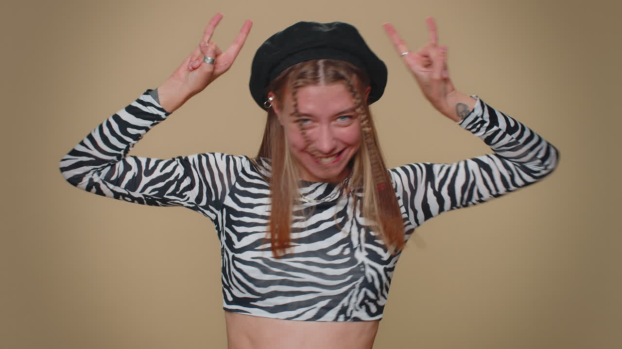 웃고, 기하고, 기하며, 예쁜 여자가 록 앤 롤 제스처를 보여주고, 춤을 추고, 감정적으로 성공을 기합니다.