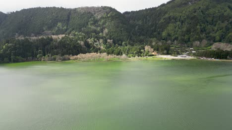 Static-aerial-view-of-alpine-landscape-in-front-of-a-lake-with-green-reflections