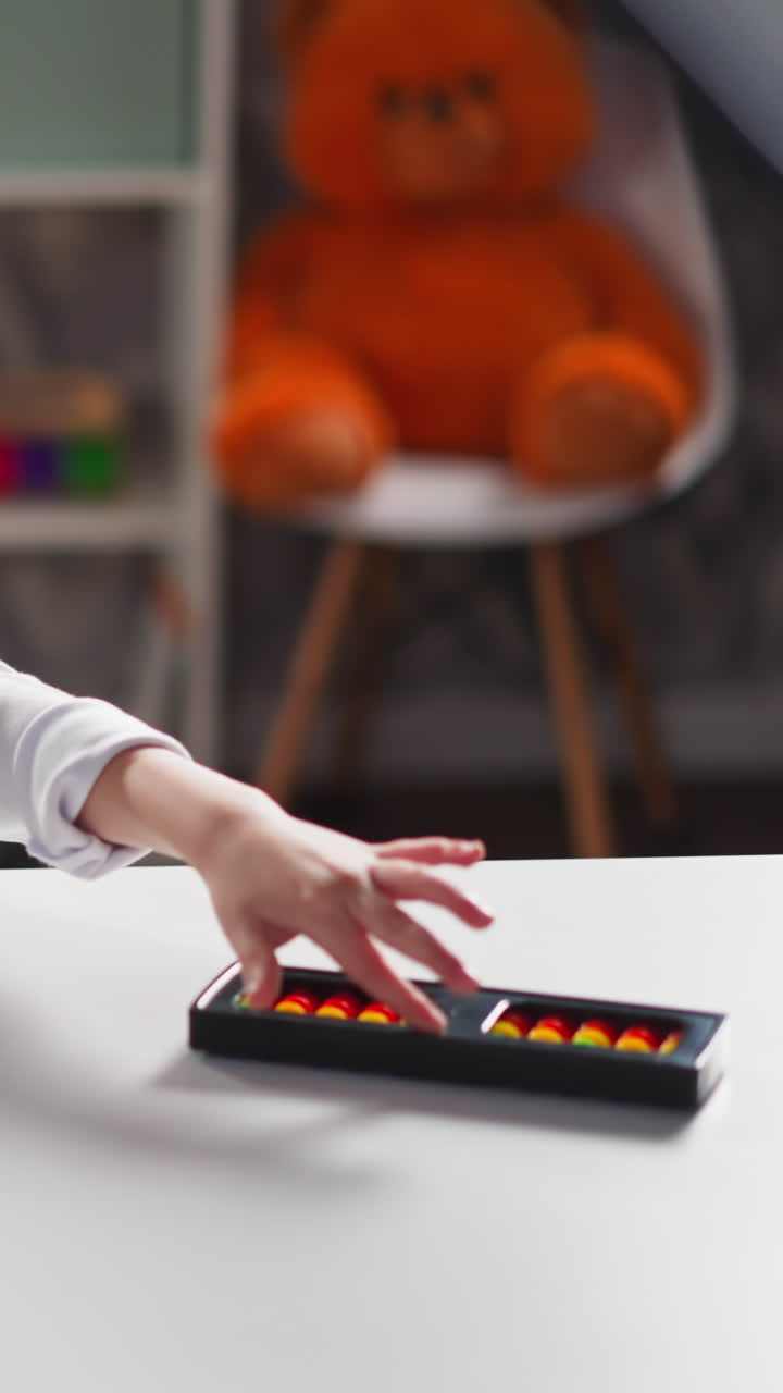 Blonde little child preschooler plays with colorful abacus sitting at white desk after uninteresting mathematics lesson close view slow motion