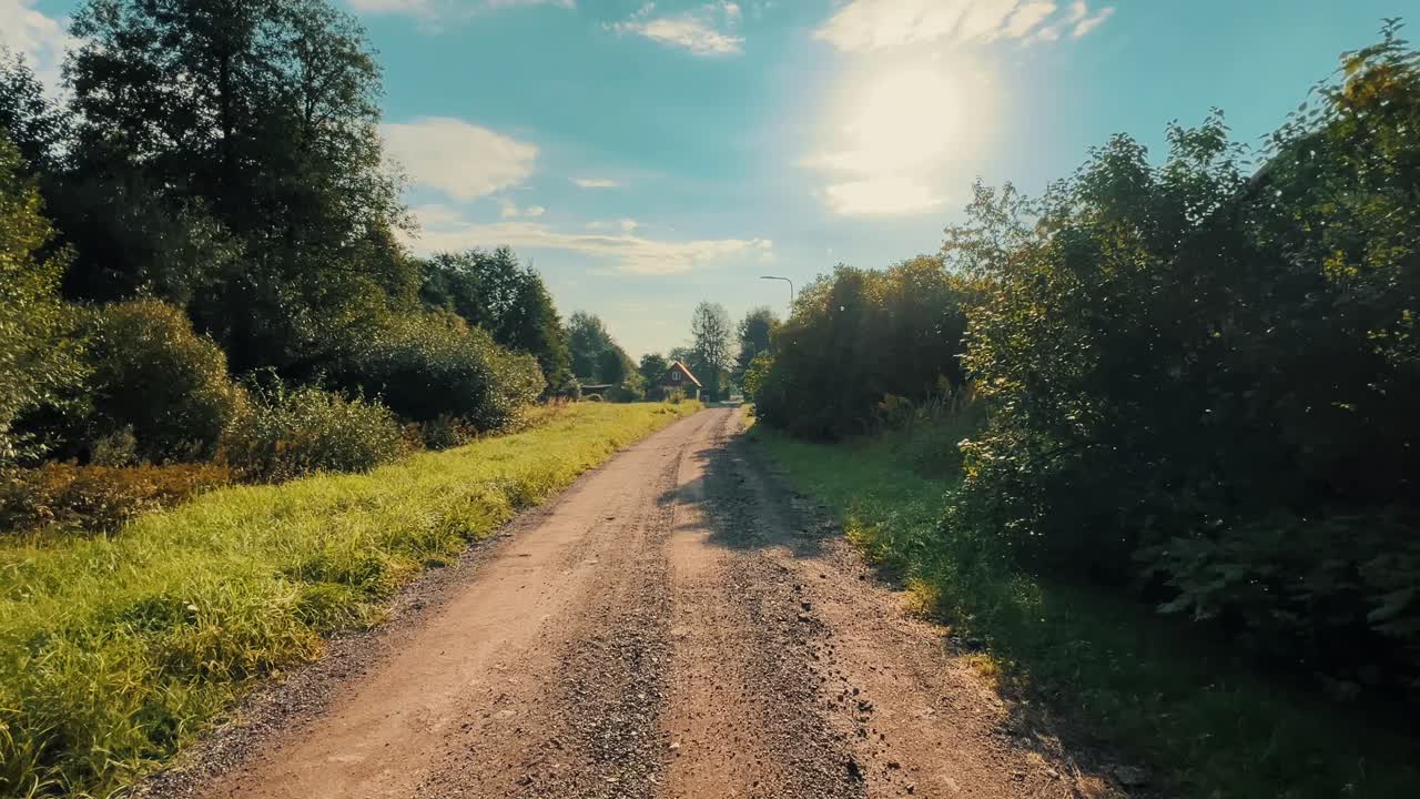 Countryside gravel path stretching into the distance under a bright sunny sky, surrounded by vibrant green grass and trees, offering a tranquil natural setting