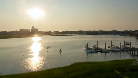 4k overhead shot of waterway as paddle boarders paddle together near a small beach town at sunrise