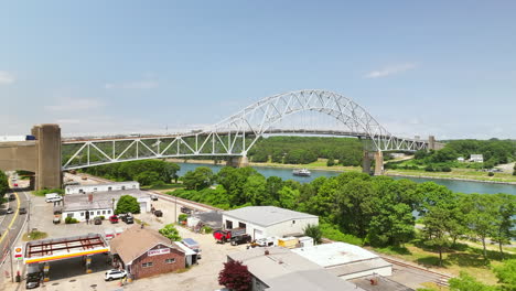 boat crosses cape cod canal under sagamore bridge, lush green landscape background, aerial view