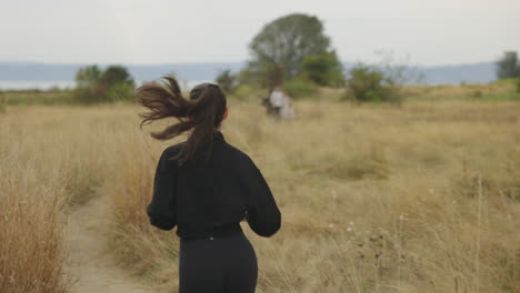 rear profile of a athletic caucasian woman jogging in black clothing through a field as her ponytail bounces