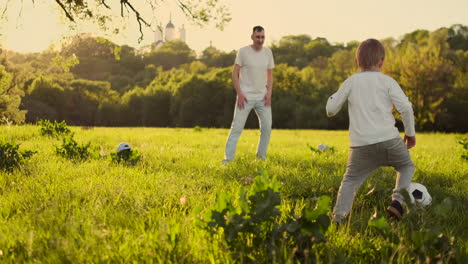 Young-father-with-his-little-son-playing-football-on-football-pitch