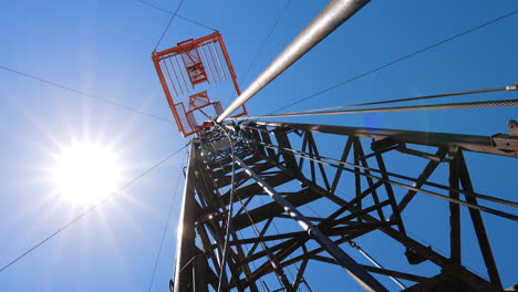 high derrick for oil drilling at the backdrop of blue sky with bright sun. low angle view at the tower for boring natural resources.