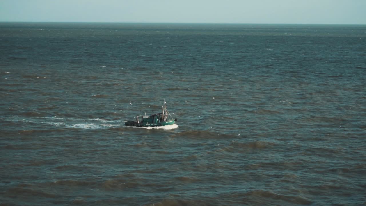 Slow motion shot of a small fishing boat sailing through the Indian ocean while seagulls follow