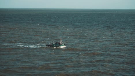 slow motion shot of a small fishing boat sailing through the indian ocean while seagulls follow