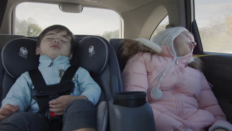 los niños que duermen conducen en el asiento trasero del coche. un bebé asiático duerme en un asiento para niños, una chica duerme a su lado.