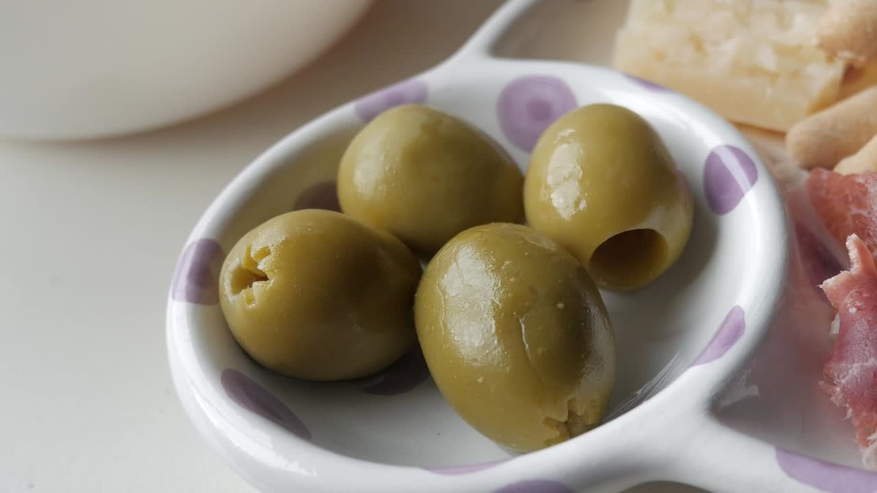 Olives served in a small dish, a part of a tapas platter with jamon, cheese, and chips