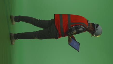 full body back view of asian male engineer with safety helmet looking at the wind turbine blueprint on a tablet while standing in the green screen background studio, during sunset or sunrise time