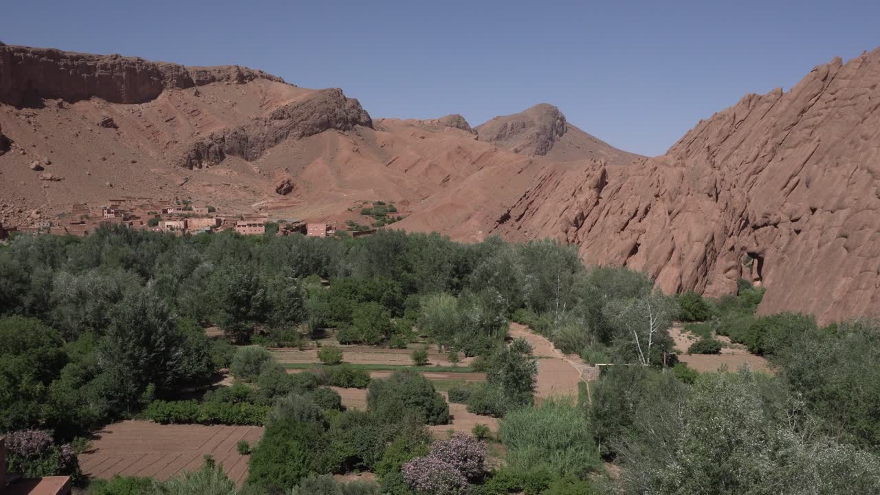 Several desert mountains under a magnificent blue sky. In the valley, you can see cultivated fields with abundant vegetation and some structures