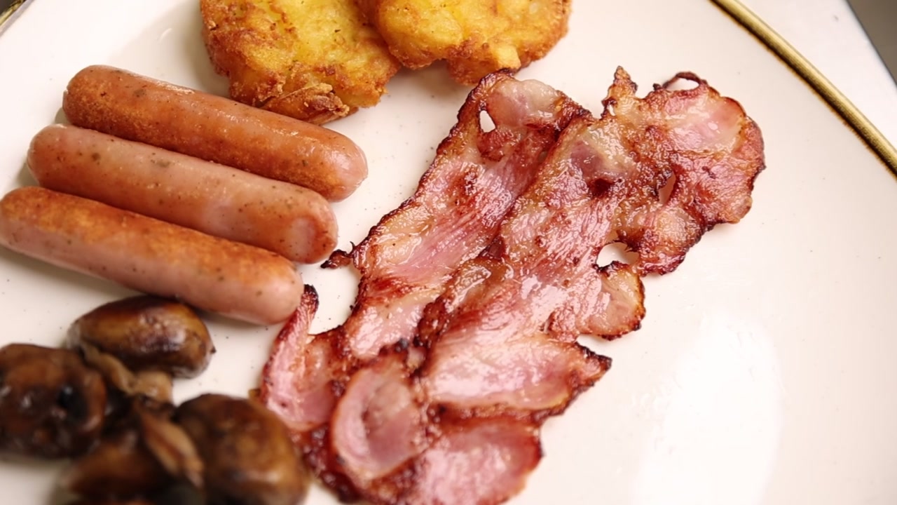 Appetitosa colazione completa con salsicce, pancetta, hash brown e funghi