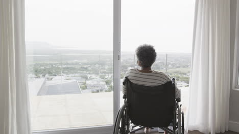 mujer afroamericana anciana en silla de ruedas junto a la ventana, espacio de copia, cámara lenta