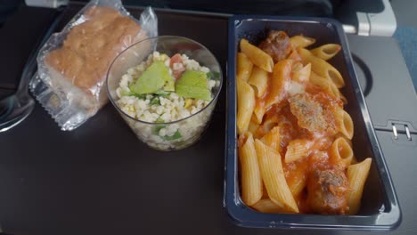 airplane meal tray with pasta, salad, and bread