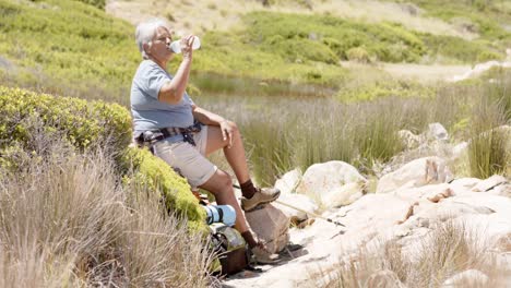 mujer biracial senior en las montañas bebiendo agua, en cámara lenta