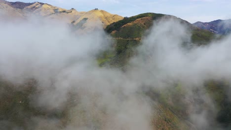 Una-Toma-Aérea-Ascendente-A-Través-De-La-Niebla-Revela-Las-Montañas-Remotas-A-Lo-Largo-De-La-Autopista-De-California-Una-Autopista-De-La-Costa-Del-Pacífico-Cerca-De-Big-Sur