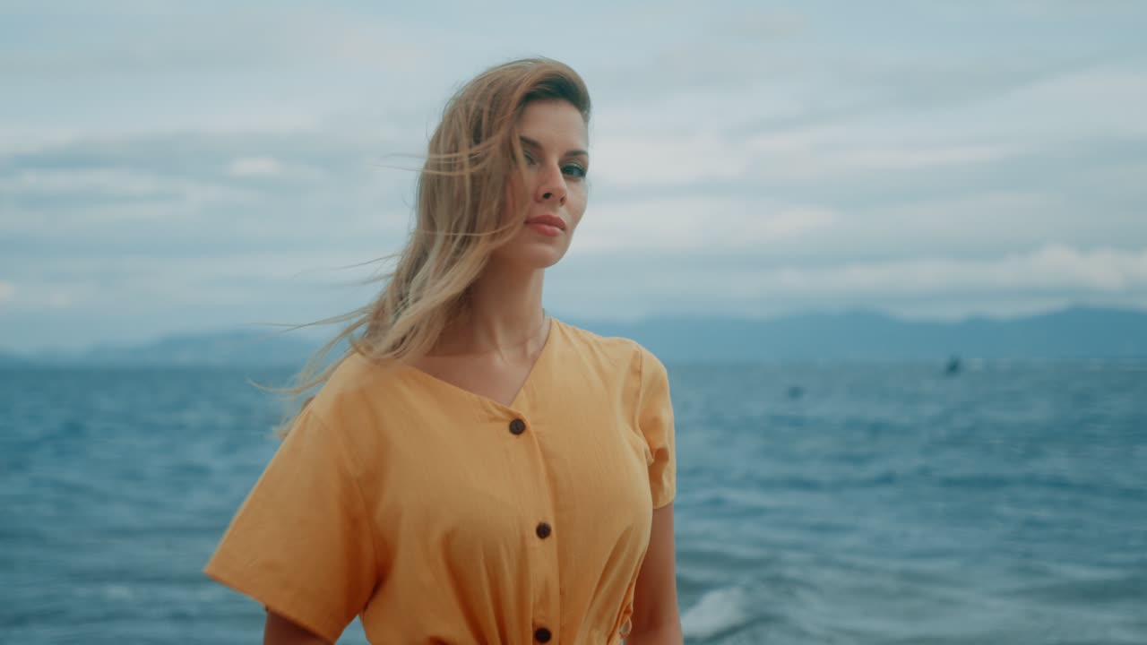 Kvinde i en gul kjole ved havet med vindblæst hår