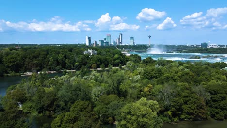 Aerial-flight-showing-splashing-niagra-waterfalls,-river-and-beautiful-skyline-in-background-during-sunny-day