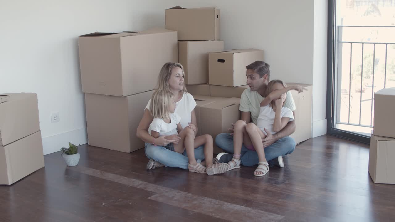 padres y dos niñas sentadas en el suelo cerca de las cajas
