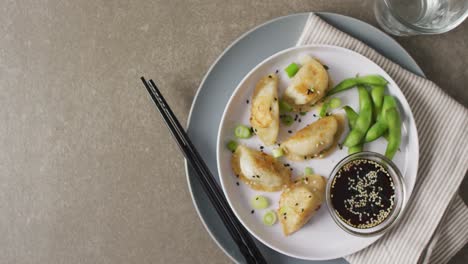 composition of plate with gyoza dumplings and soy sauce with chopsticks on grey background