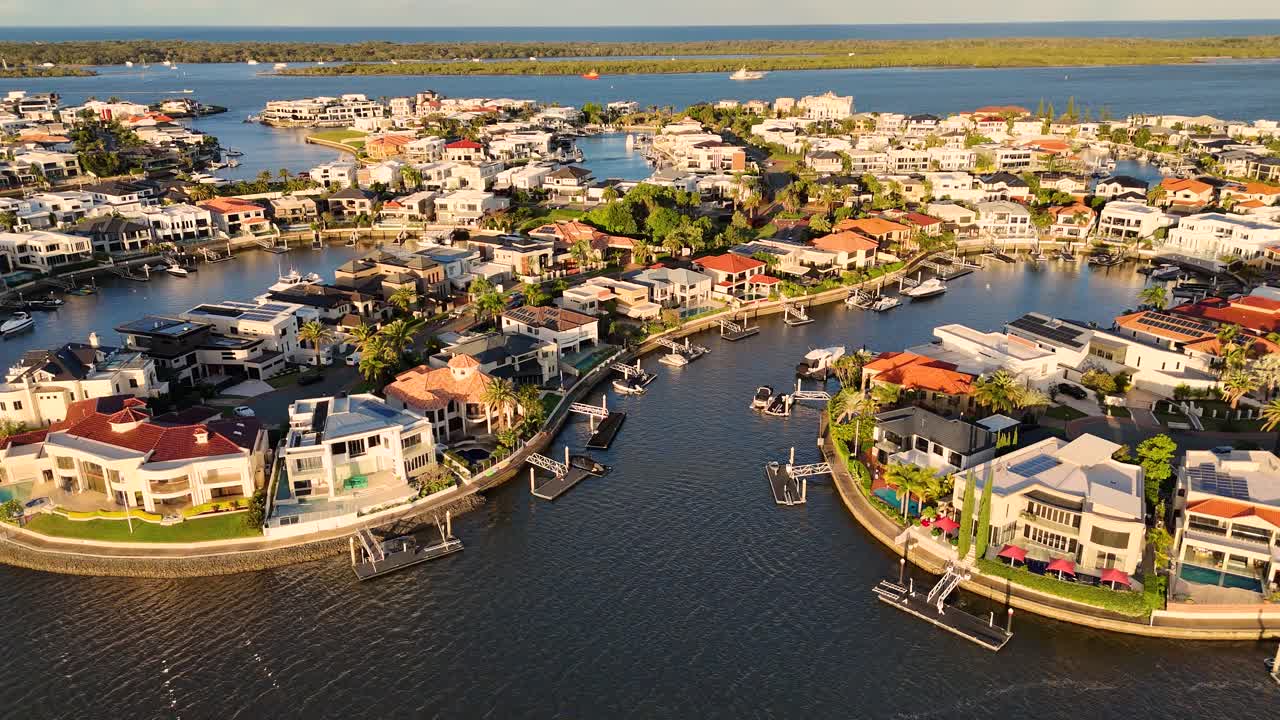 Drone footage captures luxury waterfront homes on Gold Coast, Australia, under warm sunlight with calm waters and vibrant surroundings