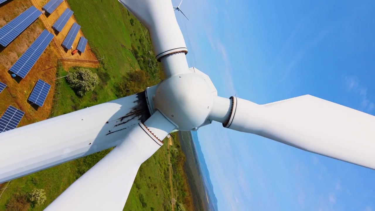 Vista aerea ravvicinata del mozzo del rotore e delle pale di una turbina eolica in campagna. Meccanismo della navicella bianca posizionato sopra campi verdi e cielo blu, prospettiva dettagliata.
