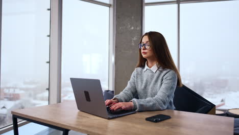 long-haired brunette sits at desk typing on her laptop. businesswoman working in the spacious office.
