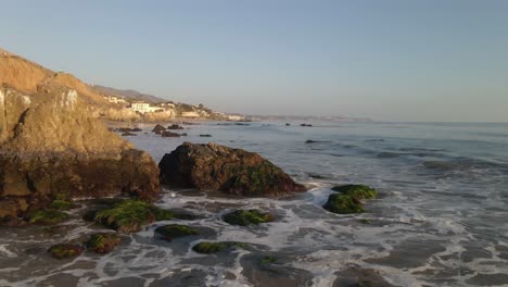 cinematic aerial footage of waves rolling into the shore at el matador beach, malibu california during golden hour