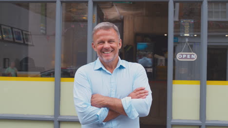 portrait of male owner or staff standing outside coffee shop folding arms