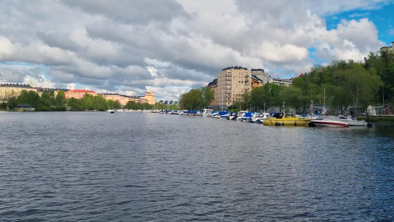 View over Karlbergssjön in central Stockholm, Sweden, with anchored boats and distant houses under a cloudy spring sky, capturing calm urban waterfront life