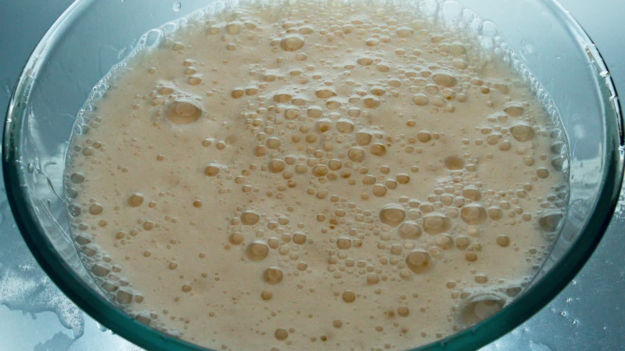Superficie di birra lager schiumosa, vista dall'alto. Bolle di bevanda alcolica che scoppiano lentamente.