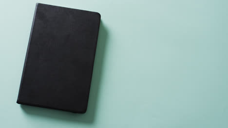 Close-up-of-closed-black-book-with-copy-space-on-green-background-in-slow-motion