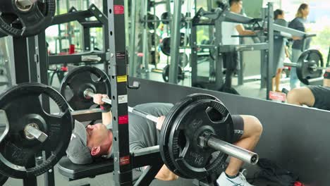 a man performs a barbell bench press in a well-equipped gym, showcasing strength and focus. bright lighting enhances the energetic atmosphere