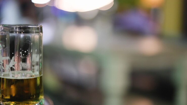 Un bicchiere di birra è appoggiato su un tavolo in un vivace e sfocato ambiente stradale con illuminazione vibrante e movimento dinamico dello sfondo.