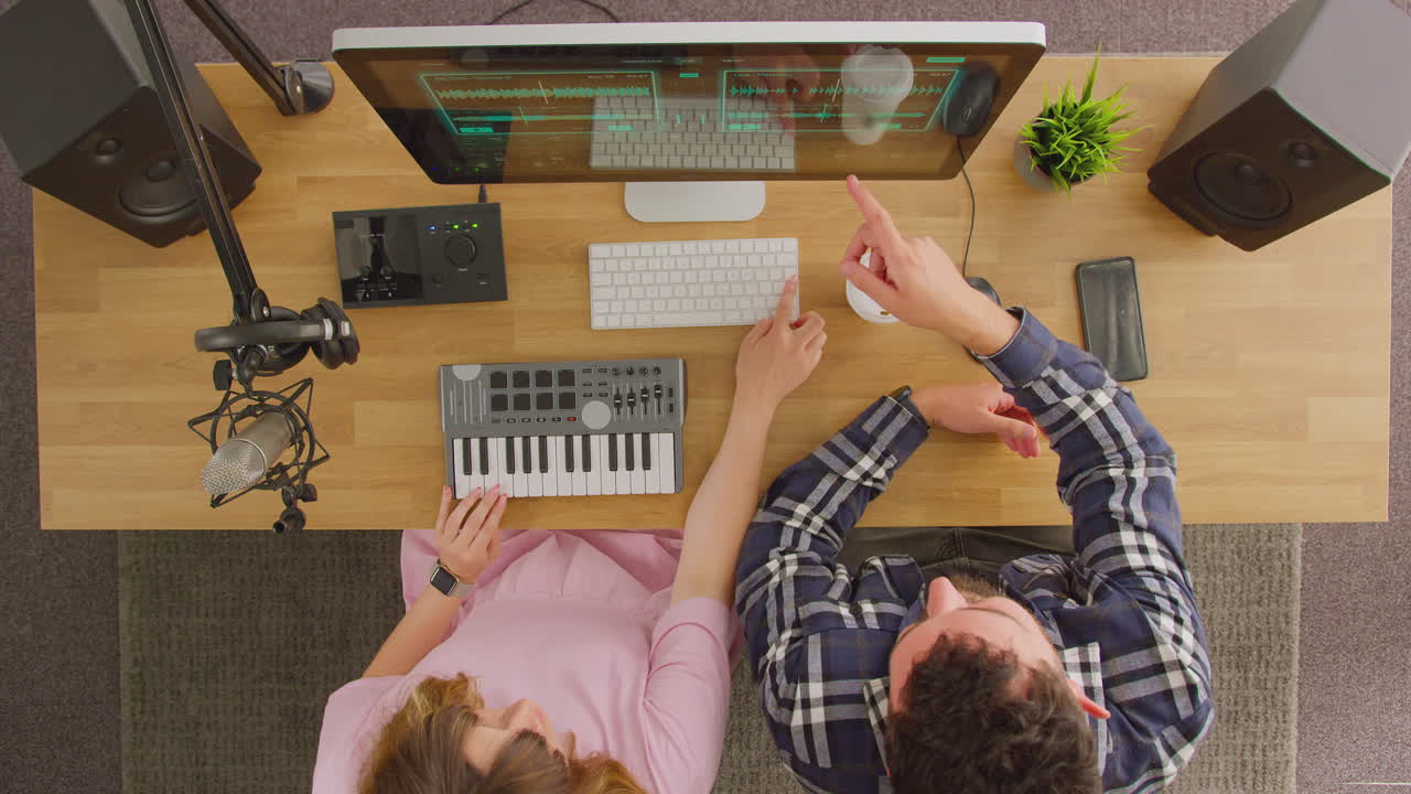 Overhead View Of Male And Female Musicians At Workstation With Keyboard And Microphone In Studio