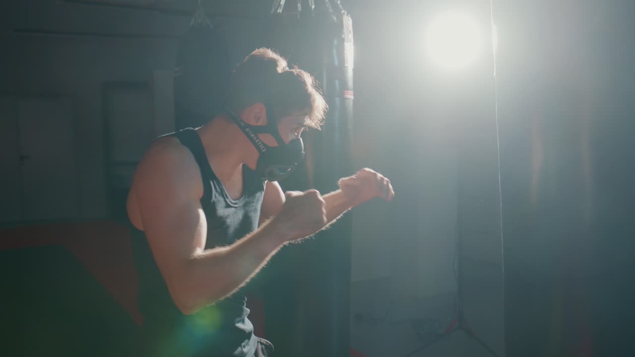 Man in Training Mask Boxing with Punching Bag in Dark Gym