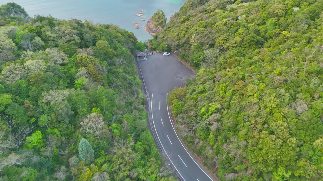 An aerial shot pulls back to reveal a secluded lodge with a red roof, nestled in a lush green forest. The shot showcases the stunning location of the property, overlooking a serene and coastal cove