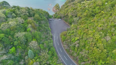 an aerial shot pulls back to reveal a secluded lodge with a red roof, nestled in a lush green forest. the shot showcases the stunning location of the property, overlooking a serene and coastal cove