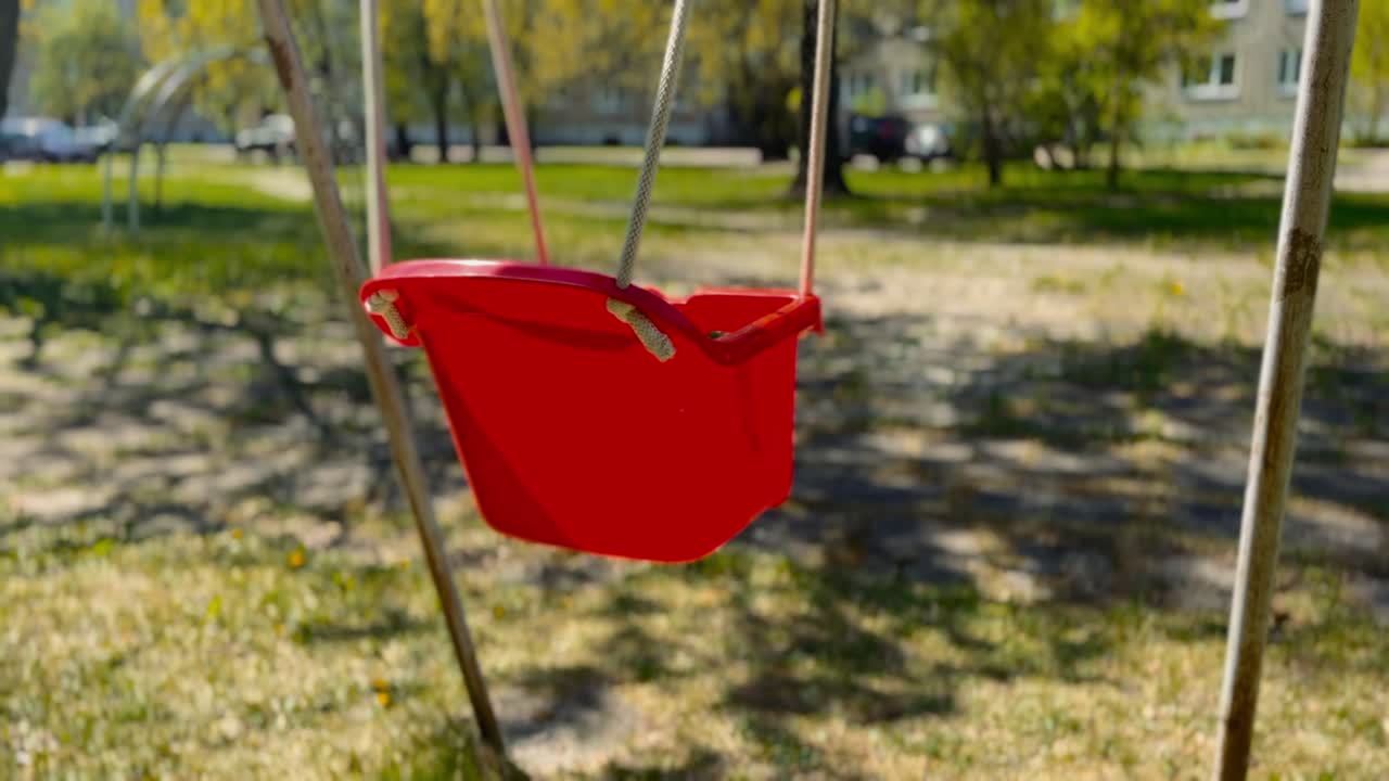 un columpio rojo vacío se mueve con el viento en un patio de recreo abandonado