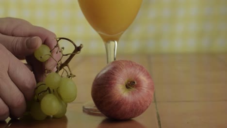 mano recogiendo uvas con manzana y vaso de jugo de naranja plano medio