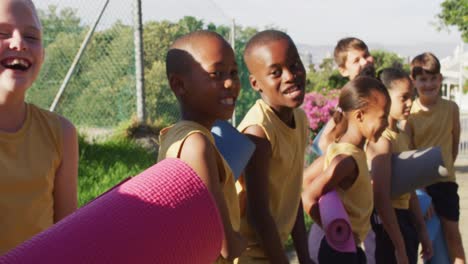 grupo diverso de escolares de pie sosteniendo esteras antes de la lección de yoga al aire libre