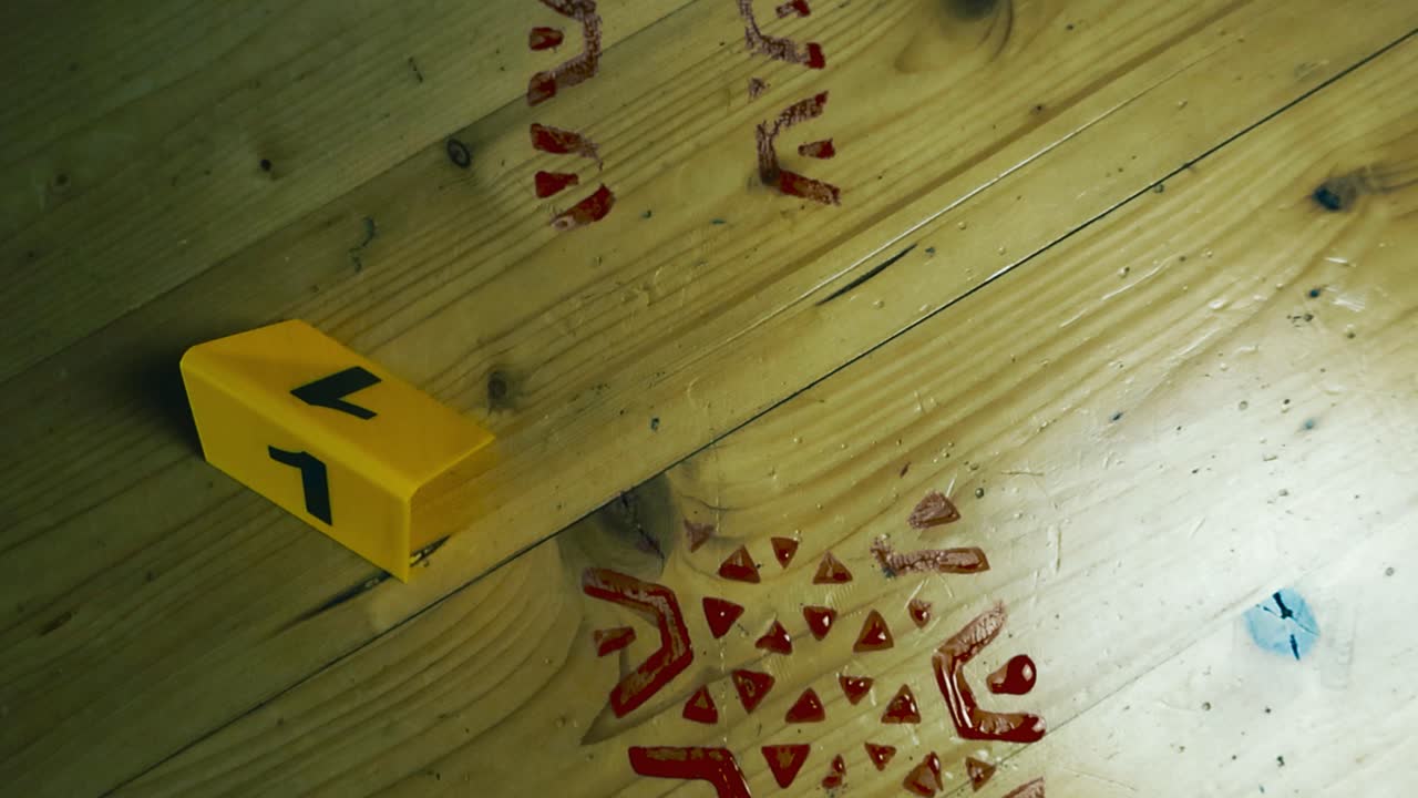 Close up video gliding over a bloody boot or footprint on a wooden pine or spruce yellow and golden colored floor inside with a yellow colored police crime scene marker placed next to it at aparment