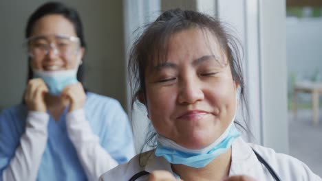 portrait of asian female nurse and patient wearing face masks, lowering masks and smiling to camera