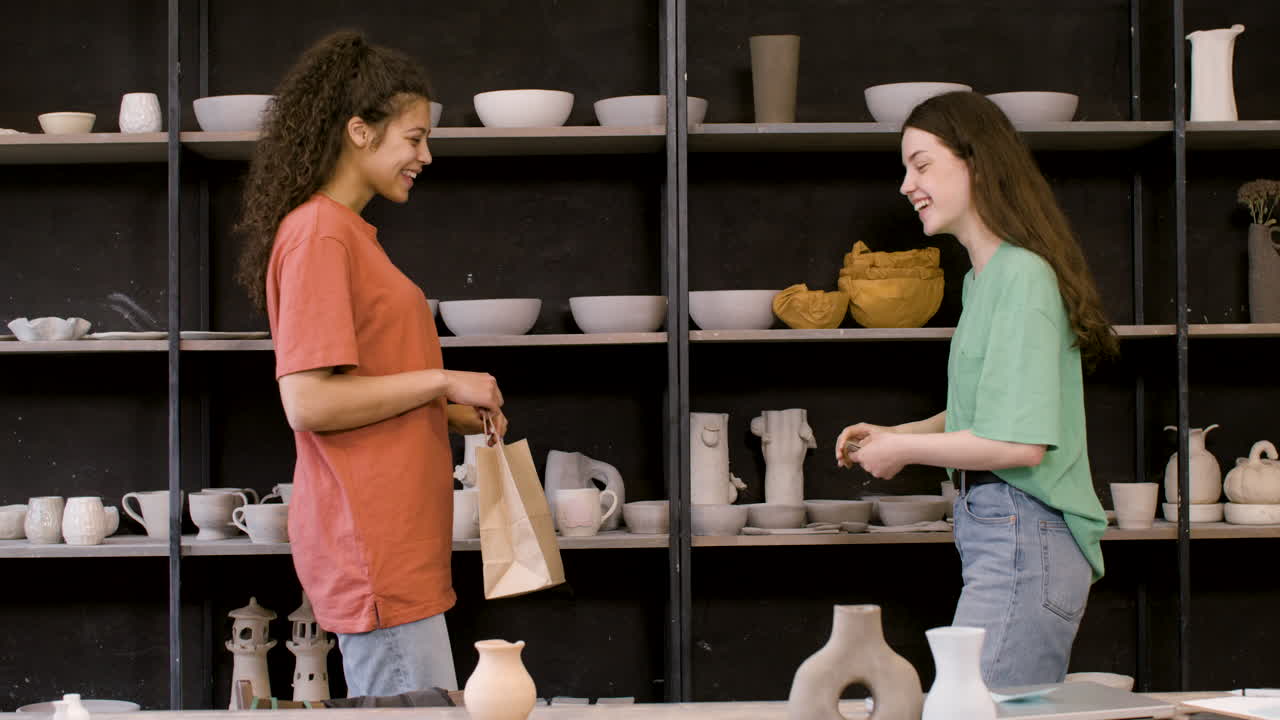 feliz dueña de un estudio de cerámica dando una bolsa de compras a una clienta que paga en efectivo
