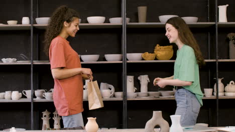 feliz dueña de un estudio de cerámica dando una bolsa de compras a una clienta que paga en efectivo