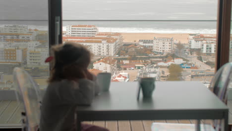 vista matutina de un niño esperando el desayuno con el teléfono playa del océano en el fondo