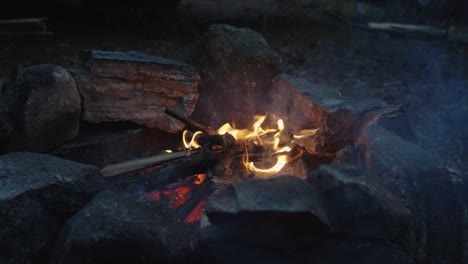 bright orange flames licking up in the air, slow motion shot of small campfire burning wood surrounded by stones, 4k wide shot