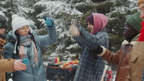 young joyful tourists dancing at campsite in winter forest