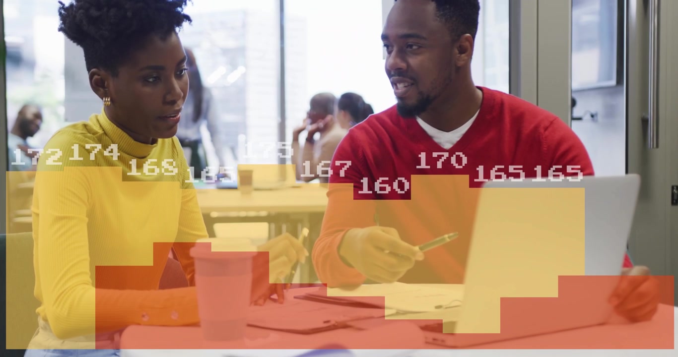 Man pointing at laptop, woman writing, animated business charts appearing over table, collaborating
